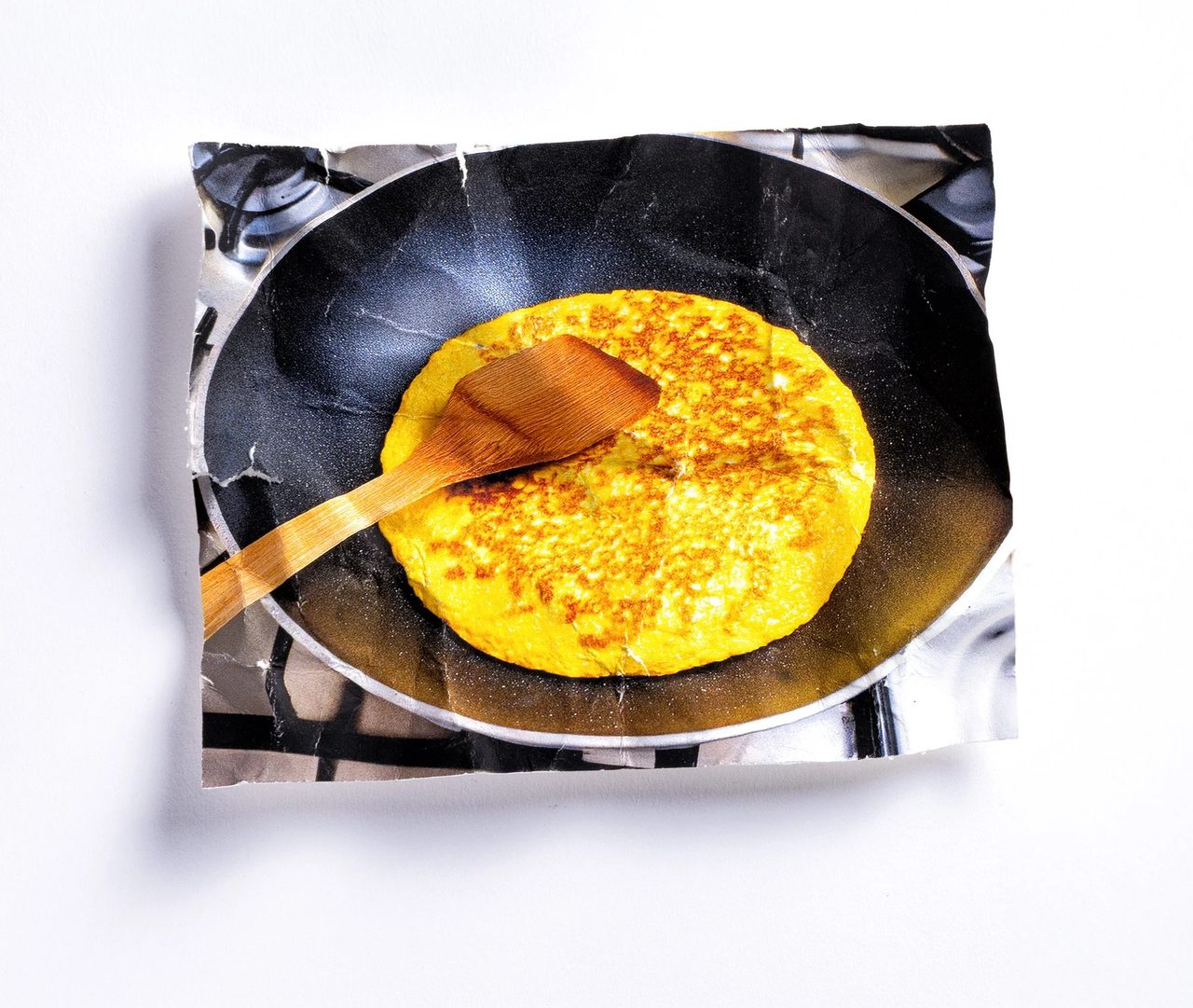 Stampa fotografica accartocciata con una frittata in padella antiaderente su fornello a gas — immagine AI stampata e accartocciata, fotografata su sfondo bianco